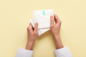 Female hands with menstrual pads on yellow background