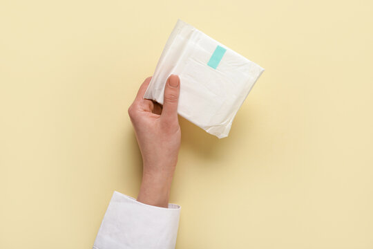 Female hand with menstrual pad on yellow background
