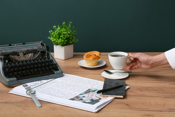 Female hand holding cup of coffee with newspapers and vintage typewriter on wooden table