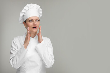 Surprised woman chef in uniform on grey background, space for text