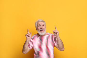 Senior man with mustache pointing at something on orange background