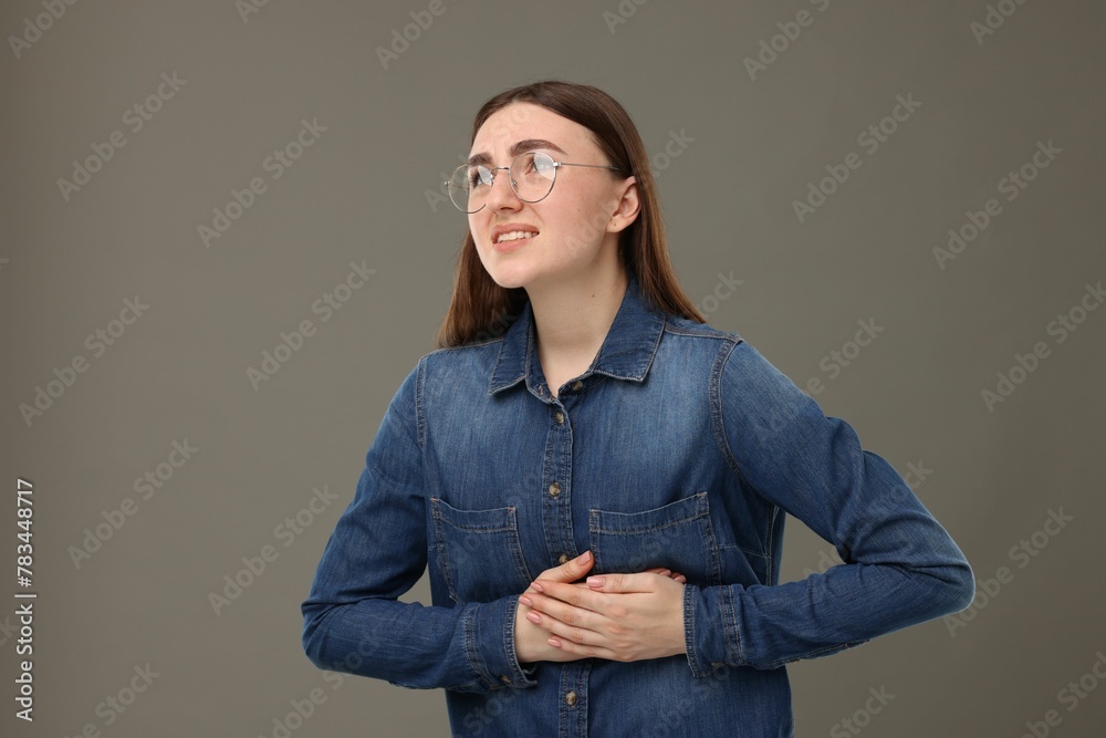 Wall mural Woman suffering from stomach pain on grey background