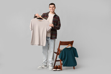Handsome young man and chair with clothes on grey background