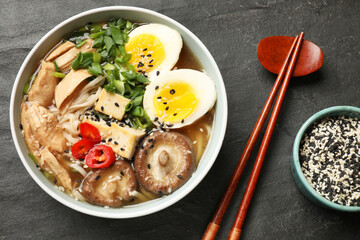 Noodle soup. Bowl of delicious ramen, ingredients and chopsticks on black table, top view