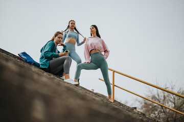 Three young fitness enthusiasts rest and chat on outdoor stairs after a workout, showcasing a...