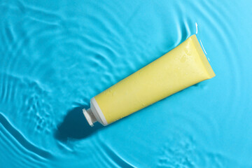 Tube with moisturizing cream in water on light blue background, top view