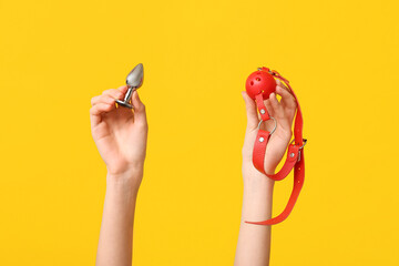 Female hands with anal plug and gag on yellow background, closeup