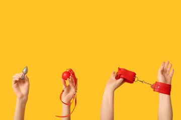 Female hands with toys from sex shop on yellow background - obrazy, fototapety, plakaty