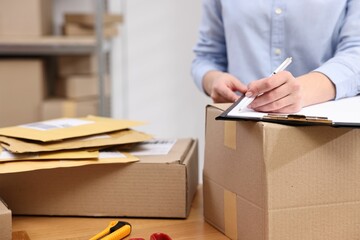 Parcel packing. Post office worker with clipboard writing notes at wooden table indoors, closeup