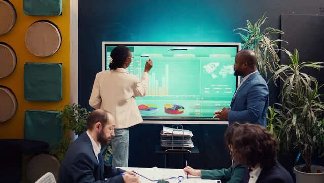 Startup team analyzing worldwide sales and client feedback, using interactive boar to examine revenue and funds. Coworkers developing brand differentiation strategies for profit growth. Camera B.