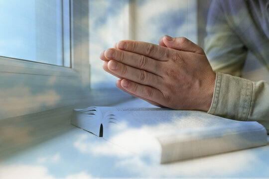 Religion. Double exposure of sky and Christian man praying over Bible at windowsill, closeup