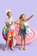 Cute little kids with inflatable mattresses and starfishes taking selfie on lilac background - obrazy, fototapety, plakaty