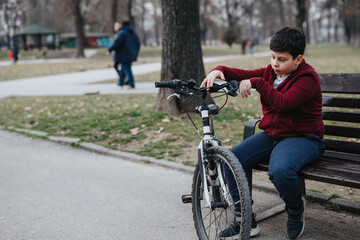 A joyful young kid rests on a bench with his bike in the park, reflecting an active lifestyle outdoors.