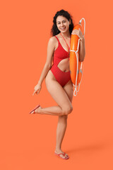 Beautiful young happy African-American female lifeguard with ring buoy on orange background