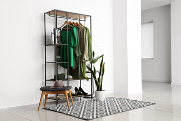 Rack with stylish female clothes, shoes and houseplant in interior of light room - obrazy, fototapety, plakaty