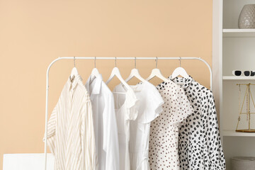 Stylish female clothes hanging on rack near color wall