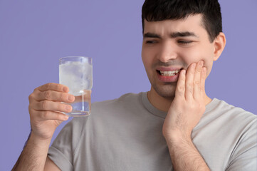 Young man with cool water suffering from toothache on lilac background, closeup