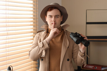 Male spy with binoculars showing silence gesture in office