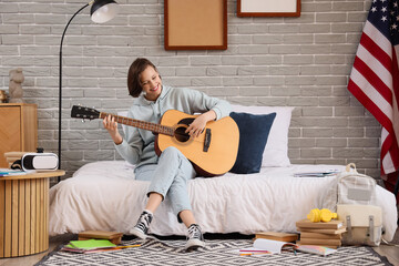 Female student playing guitar in bedroom