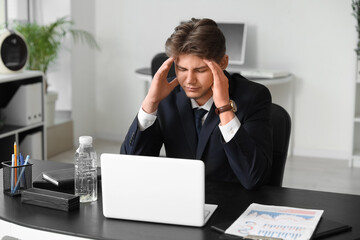 Tired young businessman suffering from headache in office