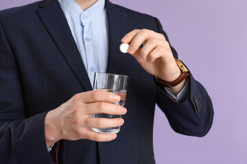 Businessman with soluble tablet and glass of water suffering from headache on lilac background, closeup