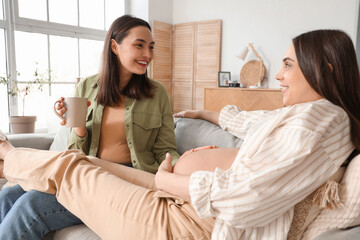 Young pregnant lesbian couple resting on sofa at home