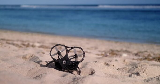 On the beach near the ocean there is an FPV drone lying on the sand, which lost its signal and fell down. The aerial drone is broken. Restoration and repair of electronics.