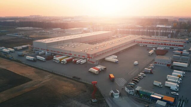 Aerial view of large warehouses and loading docks. Semi-trucks and trailers maneuver, backing up to docks for load or unload goods at the ramps