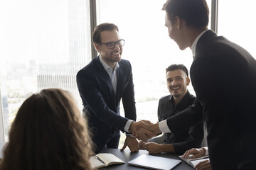 Two happy businessmen shaking hands during meeting in conference room, start or accomplish negotiations effectively and successfully, expressing mutual respect, making good deal, establish partnership