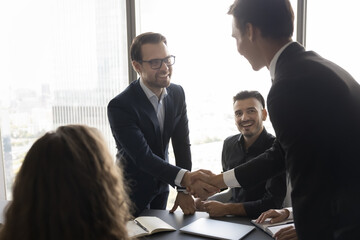 Two happy businessmen shaking hands during meeting in conference room, start or accomplish...
