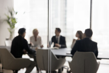 Group of businesspeople negotiating gathered in modern conference room, blurred silhouettes view,...