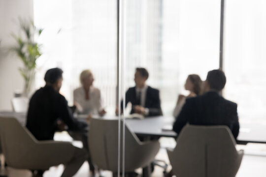 Group of businesspeople negotiating gathered in modern conference room, blurred silhouettes view, meeting behind closed glass doors. Business communication, workflow, decision-making, strategy sharing