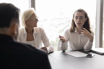 Young serious confident female employee talk to colleagues on meeting in office, solve issues,...