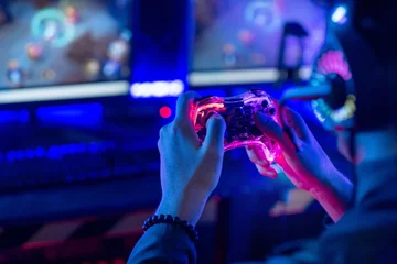 Fotobehang Gaming Close-up, video game console controller in gamer hands at colorful neon light living room at night, E-sport streaming game online, selective focus  © chomplearn_2001