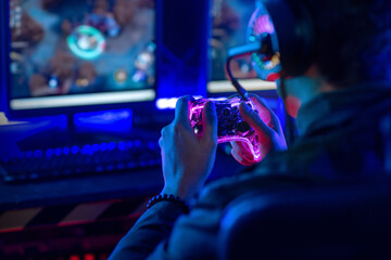 Close-up, video game console controller in gamer hands at colorful neon light living room at night,...