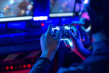 Close-up, video game console controller in gamer hands at colorful neon light living room at night, E-sport streaming game online, selective focus