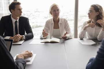 Serious business woman talk to colleagues in boardroom, hold corporate meeting, shares ideas,...