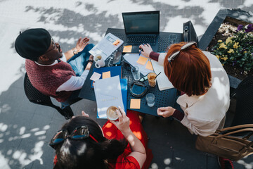 Top view of business partners in a casual meeting over coffee, discussing work with a laptop and documents.