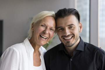 Cheerful middle-aged woman and young handsome son posing together indoor, laughing, having fun, discuss good family news, enjoying leisure carefree time at home. Ties and bonding, dental services ad - obrazy, fototapety, plakaty