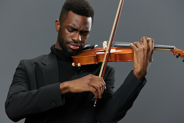 African American man in black suit playing violin against gray background in elegant musical...
