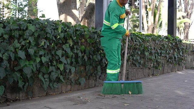 a cleaning worker who is sweeping the street in a park with a broom