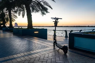 Deurstickers electric scooter on parking on the Abu Dhabi waterfront in the evening at sunset. City bike rental system, public kick scooter on the street © diy13