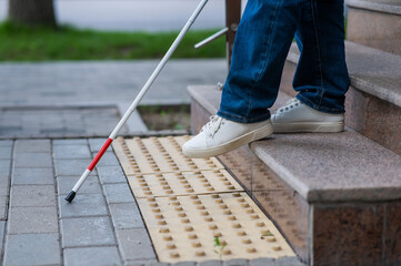 Close-up of female foot, walking stick and tactile tiles. Blind woman walking down stairs using a...