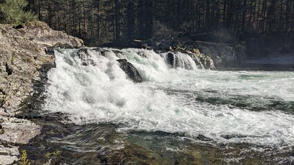 Waterfall and river winding between rocky riverbank surrounded by pine woodland. 