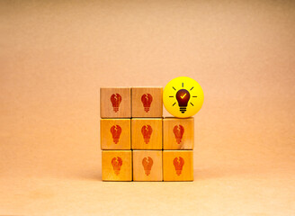 Creative idea and innovation, unique, insight, different, leadership, solutions and motivation concepts. Yellow light bulb icon on yellow ball with broken bulbs symbol on wooden cube block stack.