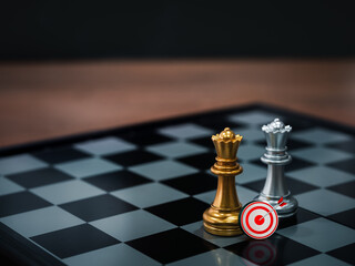 3d target icon with golden and silver queen chess pieces standing together on a chessboard on dark...