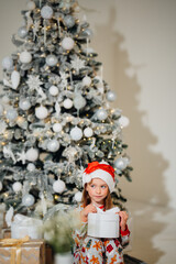 Cute little girl in pajamas with gift in box and christmas tree