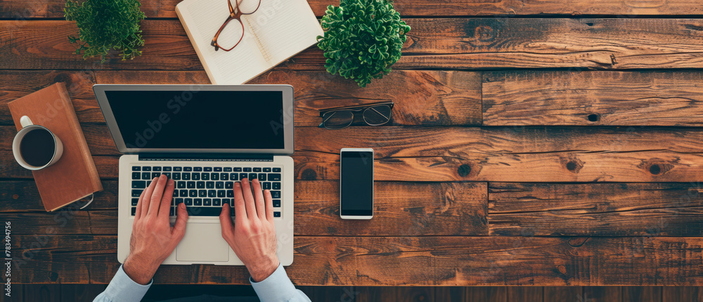 Poster overhead view of hands typing on a laptop, with a coffee cup, notebook, and smartphone on a wooden d