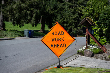 Road Work Ahead bright orange sign on the side of a street in a residential neighborhood
