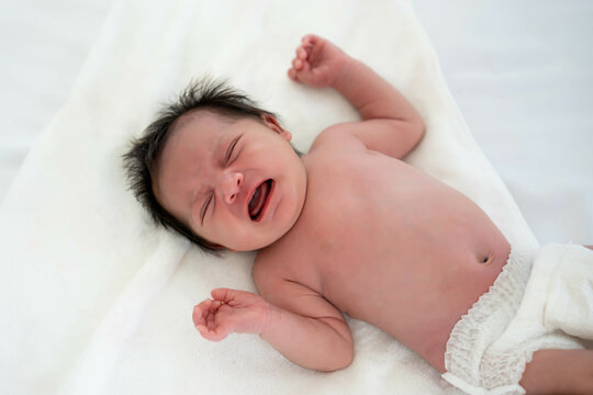 An expressive newborn baby cries while lying on a white blanket, displaying raw emotion.
